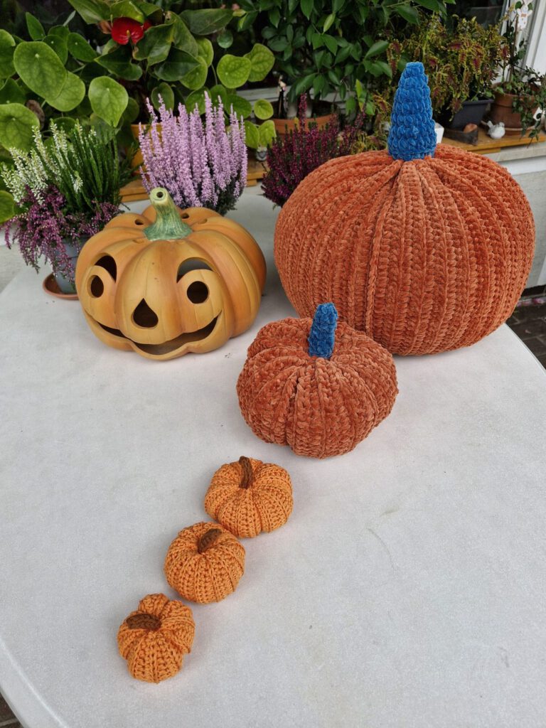 Family of crochet pumpkins in four sizes, from tiny cotton pumpkins to the XL velvet pumpkin, on a white garden table