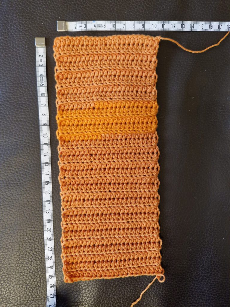 Orange crocheted rectangle in half double crochet with a measuring tape, the starting point of the free crochet pumpkin pattern