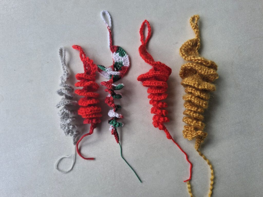 Five crocheted icicle ornaments in mustard, red, green and gray made from leftover yarn