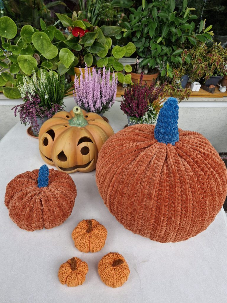 Four crochet pumpkins in different sizes in front of a ceramic jack-o-lantern on a white table