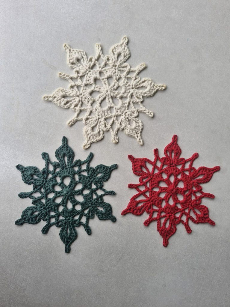 Three crocheted snowflake ornaments in cream, dark green and red cotton yarn