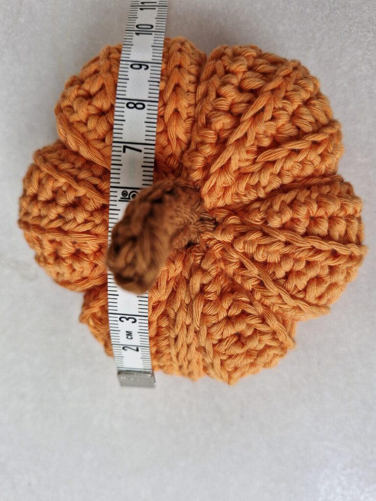Small orange crochet pumpkin seen from above with a measuring tape across it