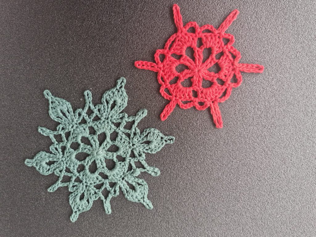 Two crocheted snowflake stars in coral red and mint green on a dark surface