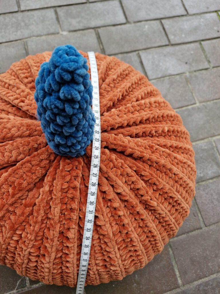 XL crochet pumpkin in burnt orange velvet yarn with a blue stem and a measuring tape on a stone floor