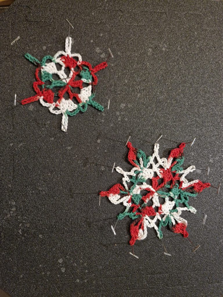 Two colorful crocheted snowflakes pinned for blocking