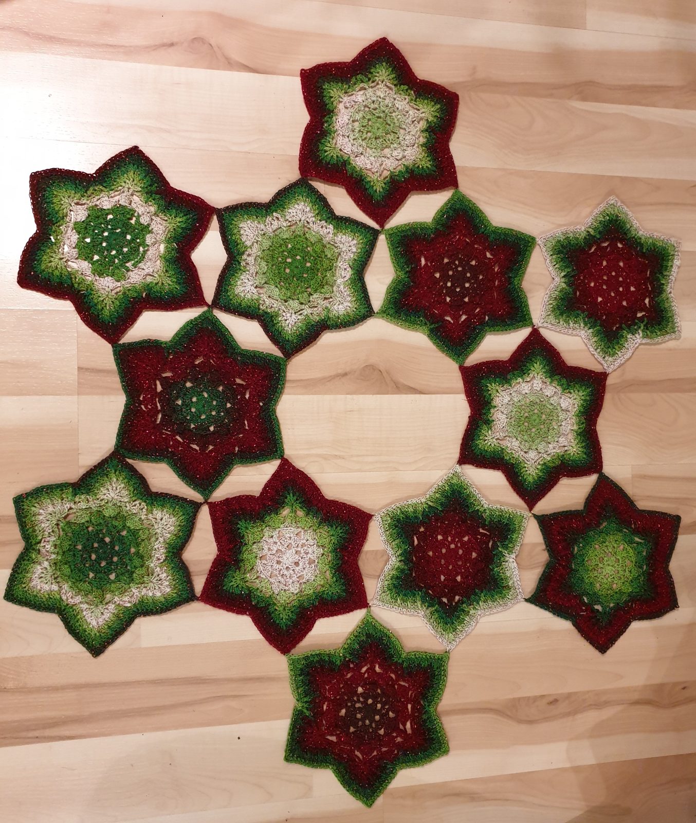 Finished crochet tree skirt made of twelve hexie stars laid out flat on a wooden floor