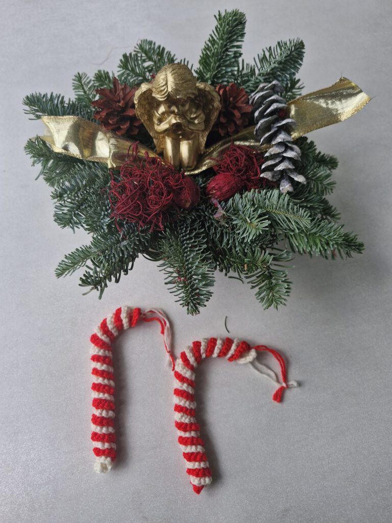 Two crocheted red and white candy cane ornaments next to a Christmas arrangement