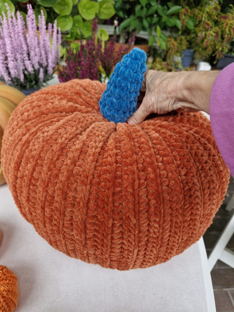 Hand on the wintergreen stem of a large burnt orange velvet crochet pumpkin