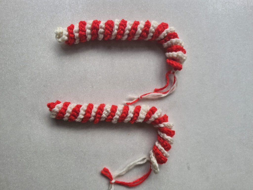 Crocheted red and white striped candy cane ornament lying flat