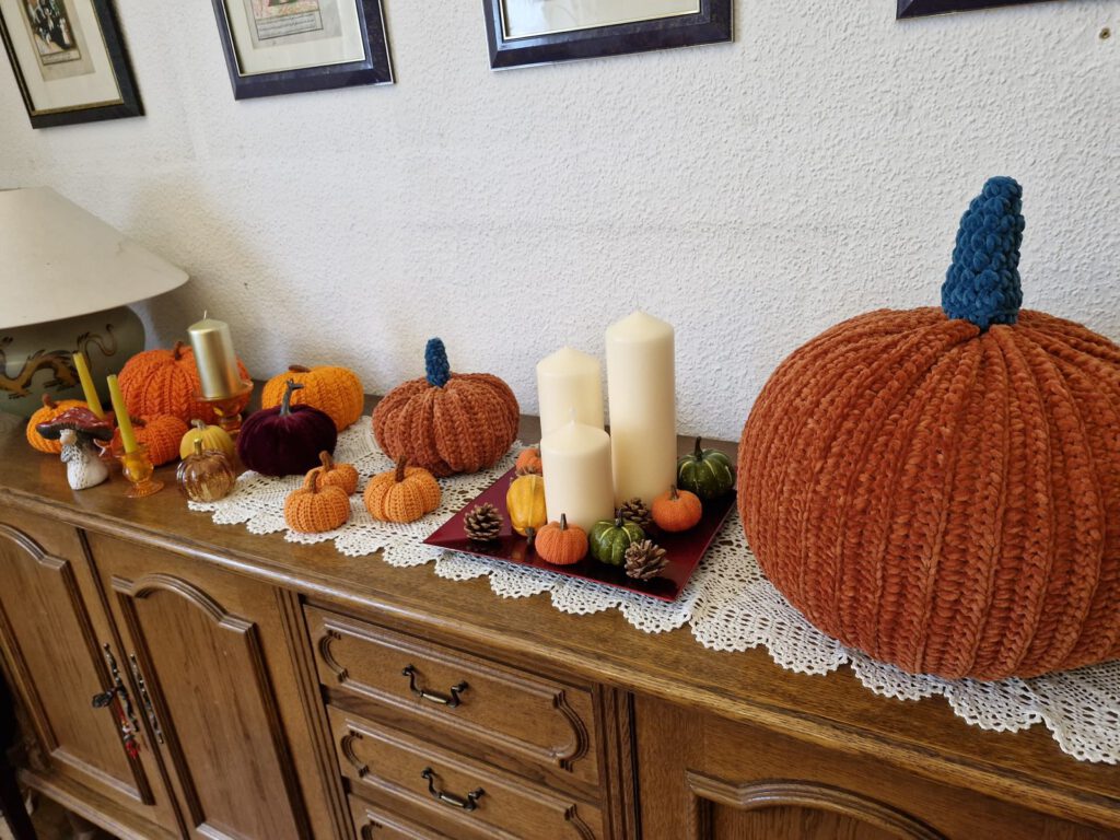 Crochet pumpkins in different sizes on a wooden sideboard with white candles as autumn decoration
