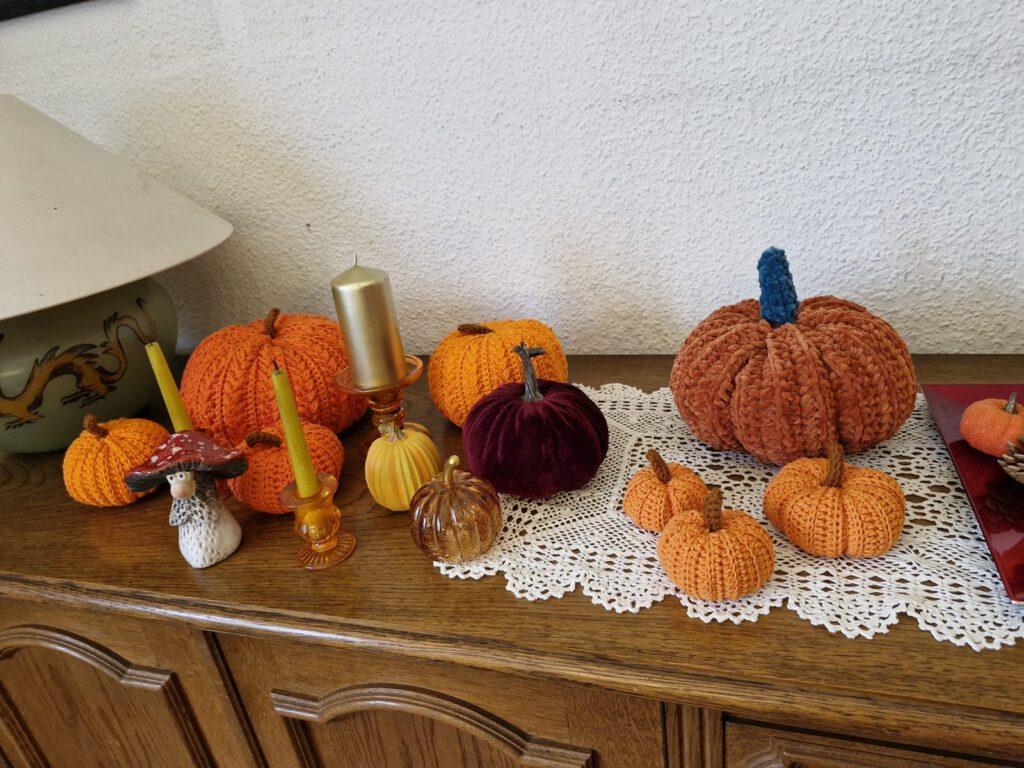 Wooden sideboard with a lace runner, candles and crochet pumpkins in orange and rust