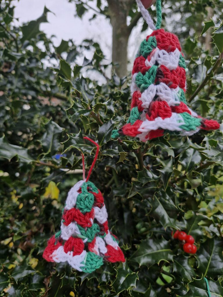 Two crocheted Christmas bells in red, green and white hanging in a holly branch